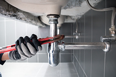 person using a wrench to repair plumbing under a sink featuring modern tiles and fixtures highlighting plumbing tools for 21st century maintenance