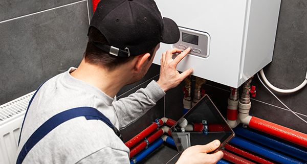 technician adjusting boiler settings with digital tablet in plumbing setup featuring eight color coded pipes