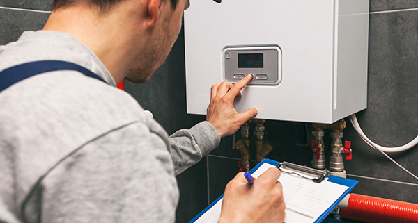 technician adjusting boiler settings while taking notes on a clipboard for two maintenance tasks