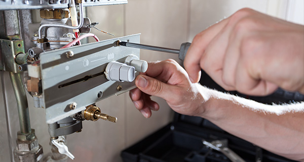 person using a screwdriver to adjust a control panel on a heating system showcasing 3 essential repairs and maintenance techniques