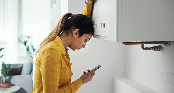 woman wearing yellow shirt looking at smartphone with head against wall in a bright room featuring a heater and indoor plants twelve ways to stay connected