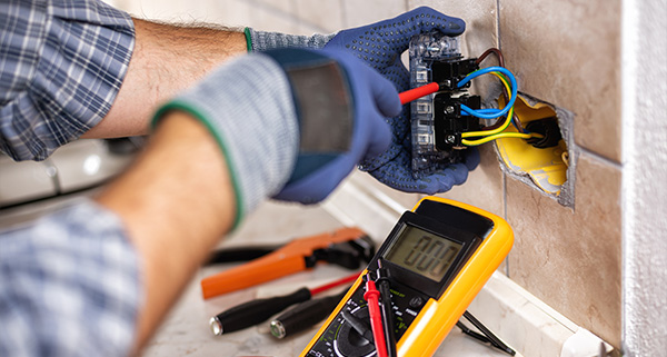 person wearing gloves working on an electrical panel with multimeter and tools showing two types of wires in a home renovation setting