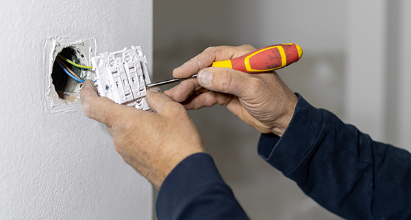 person installing a light switch using a screwdriver in a wall outlet with colored wires visible and important electrical safety tips for homeowners