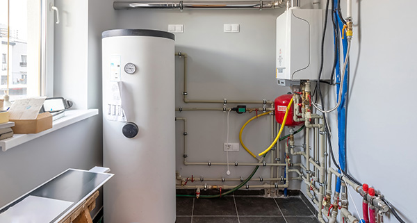 plumbing area with a hot water cylinder and various pipes connected to the wall showing an organized setup for home maintenance strategies including essential components for water heating and energy efficiency with emphasis on 12 important elements