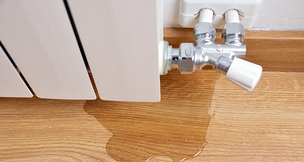leaking radiator valve with water on wooden floor near heating system in home interior maintenance issues related to 11 types of heating systems