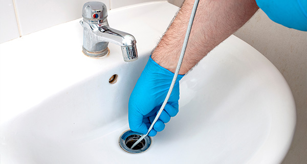 hand wearing blue gloves using a plumbing snake to clear a drain in a bathroom sink showing the faucet and sink environment 11 plumbing tips for clear drains