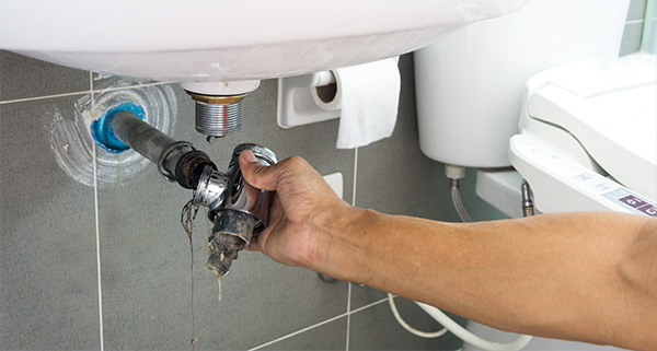 hand reaching to fix a plumbing issue under a sink showing pipes and drainage installation essential for home repairs and maintenance tips 12 common plumbing problems